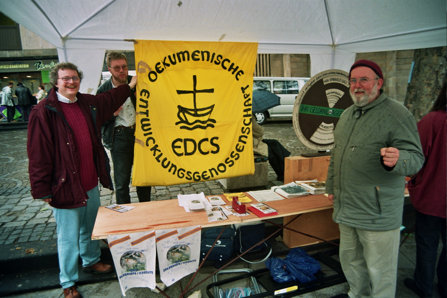 Menschen stehen vor einem Stand mit einem Banner der Ökumenische Entwicklungsgenossenschaft